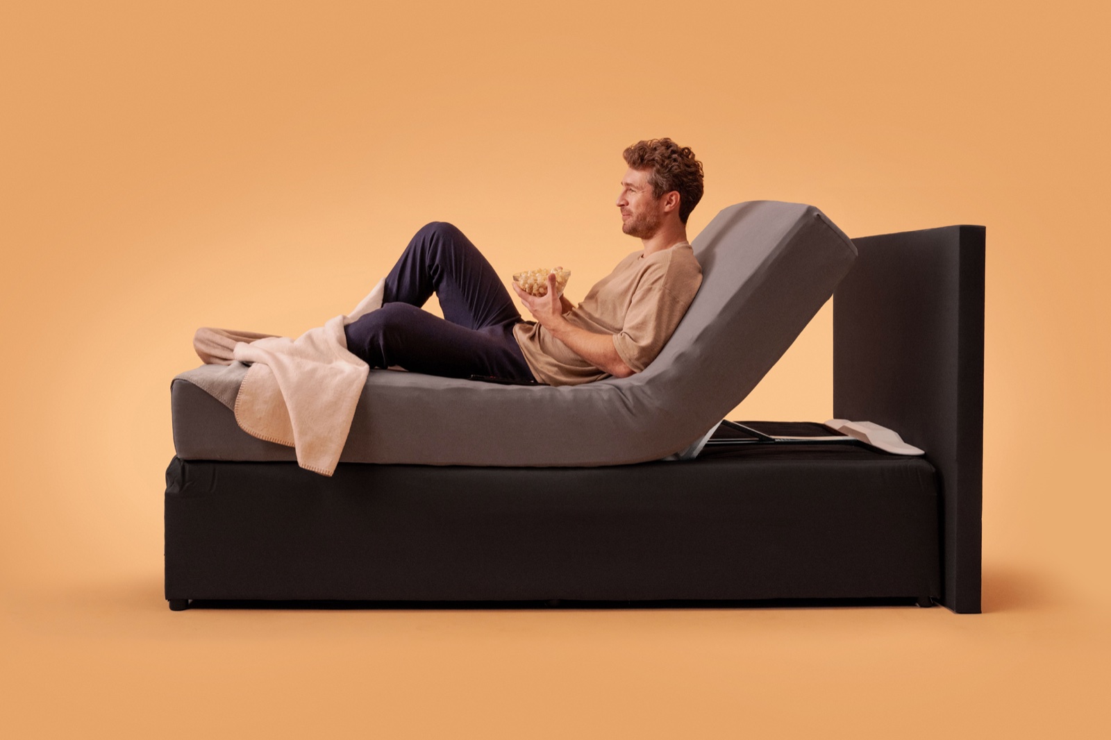 Man zit ontspannen rechtop in bed met een snack, de matras als rugleuning